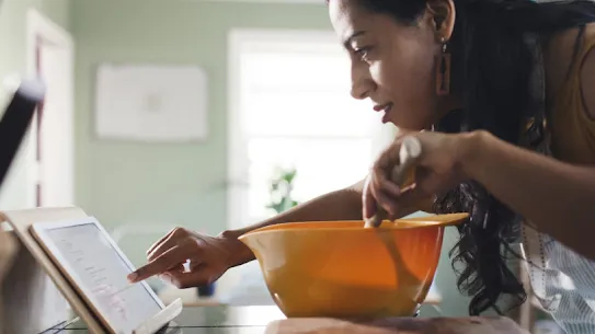 Una donna usa il suo tablet per cercare informazioni mentre cucina