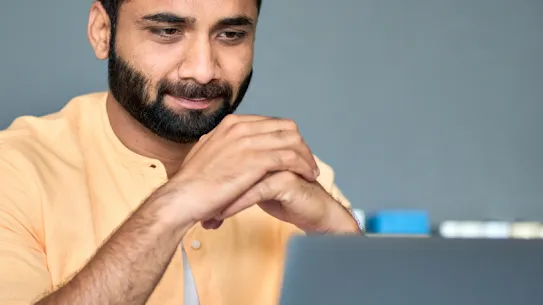 Un uomo con la barba guarda soddisfatto lo schermo di un laptop